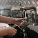 How To Increase Water Pressure in Kitchen Sink Person Pouring Water on Clear Drinking Glass